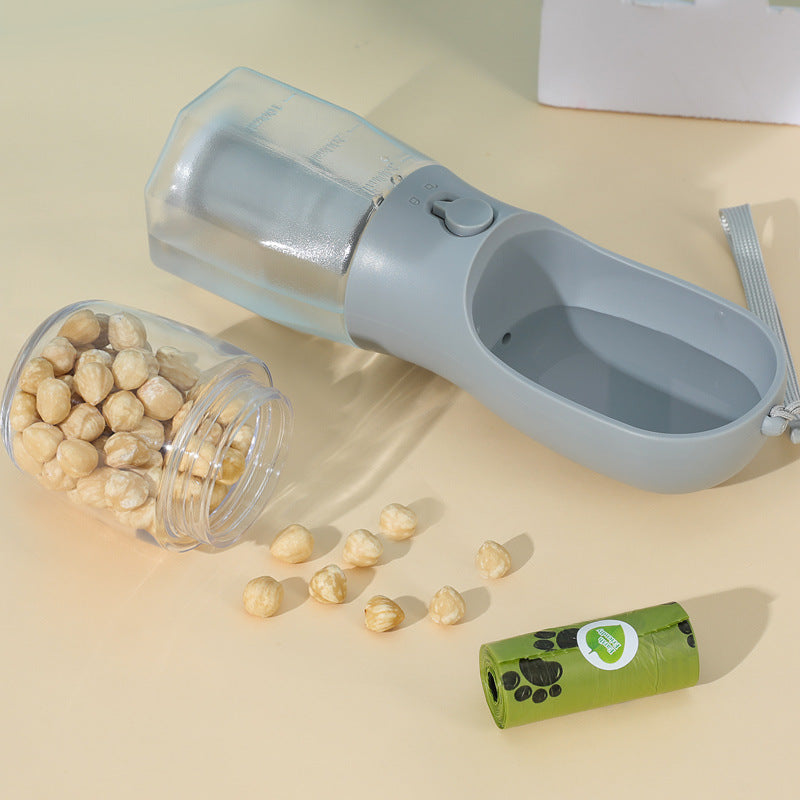 Gray 3-in-1 dog water bottle on a table with dog treats and a poop bag roll